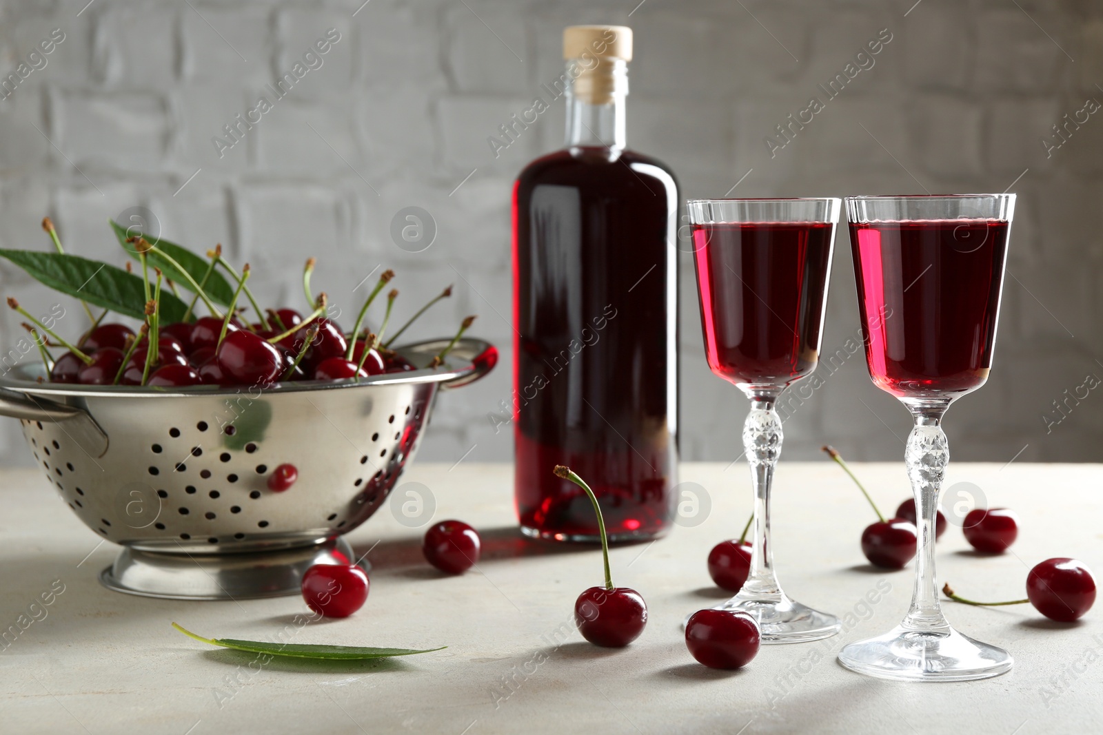 Photo of Delicious cherry liqueur in glasses, bottle and fresh berries on light grey table