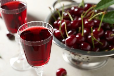 Delicious cherry liqueur in glasses and fresh berries on light grey table, closeup