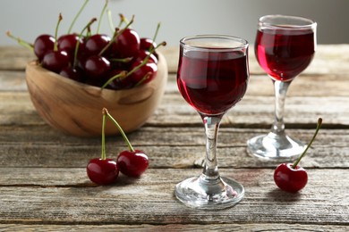 Delicious cherry liqueur in glasses and fresh berries on wooden table