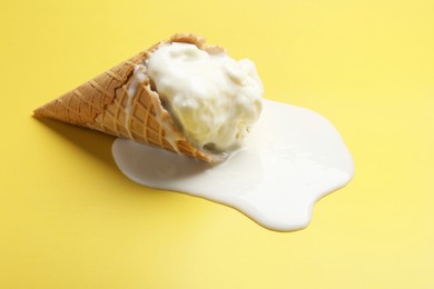 Melted ice cream in wafer cone on yellow background