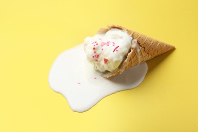 Melted ice cream in wafer cone on yellow background