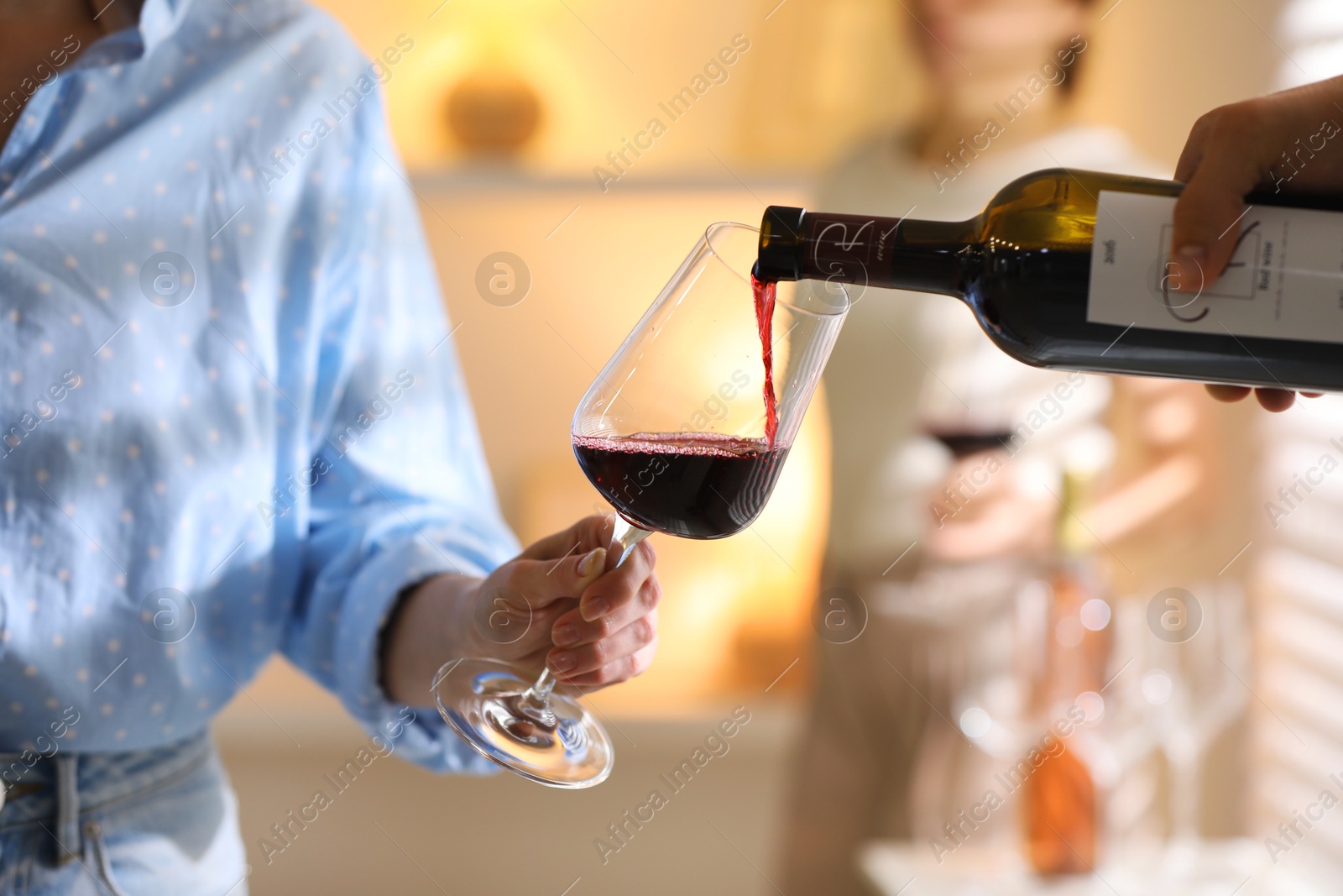 Photo of Man pouring red wine into woman`s glass indoors, selective focus