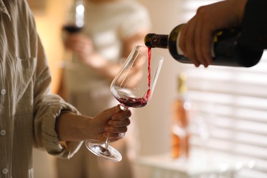 Man pouring red wine into woman`s glass indoors, selective focus