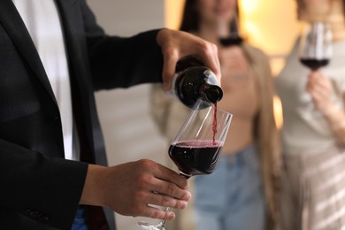 Photo of Man pouring red wine into glass indoors, selective focus