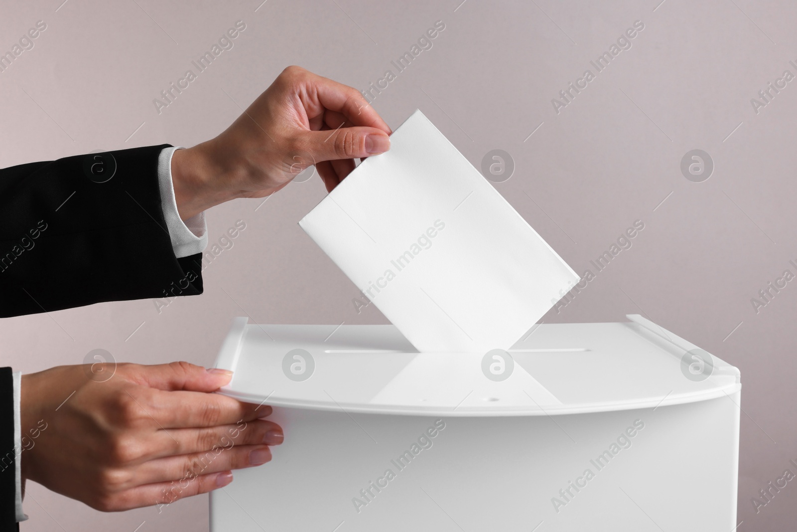 Photo of Woman putting her vote into ballot box against grey background, closeup