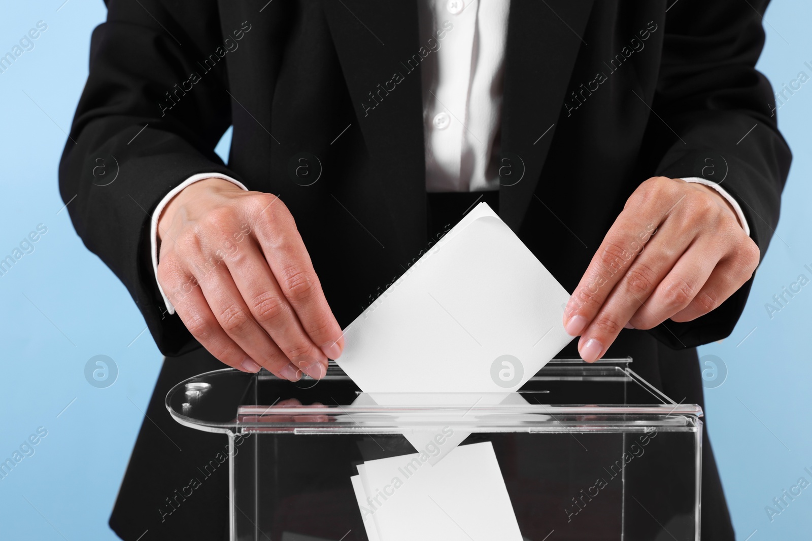 Photo of Woman putting her vote into ballot box against light blue background, closeup