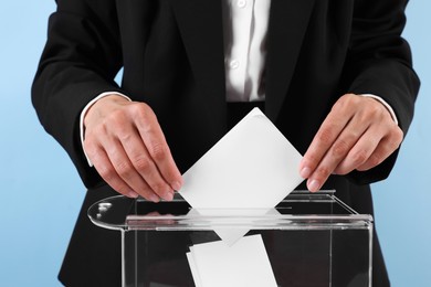 Photo of Woman putting her vote into ballot box against light blue background, closeup