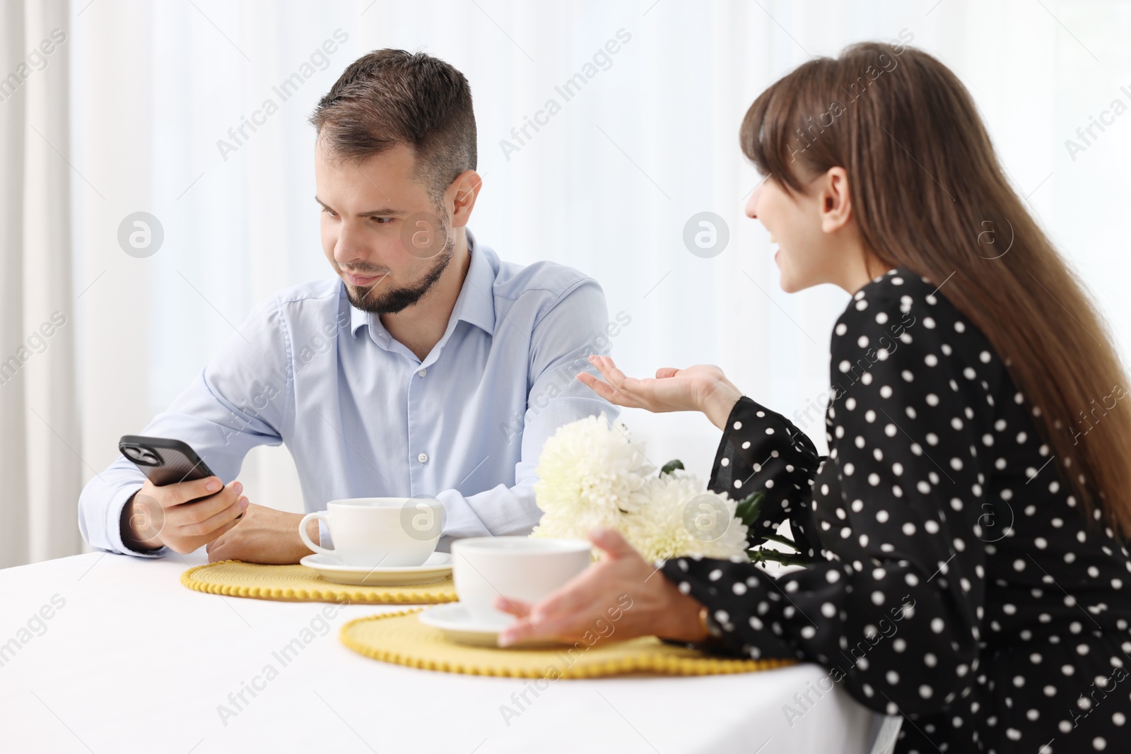 Photo of Embarrassing date. Obsessive woman talking to man with smartphone at table indoors