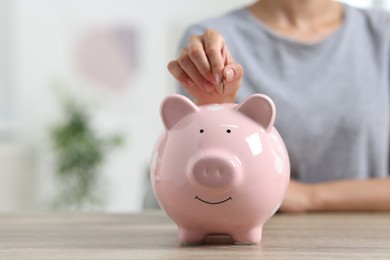 Photo of Woman putting coin into piggy bank at wooden table, closeup