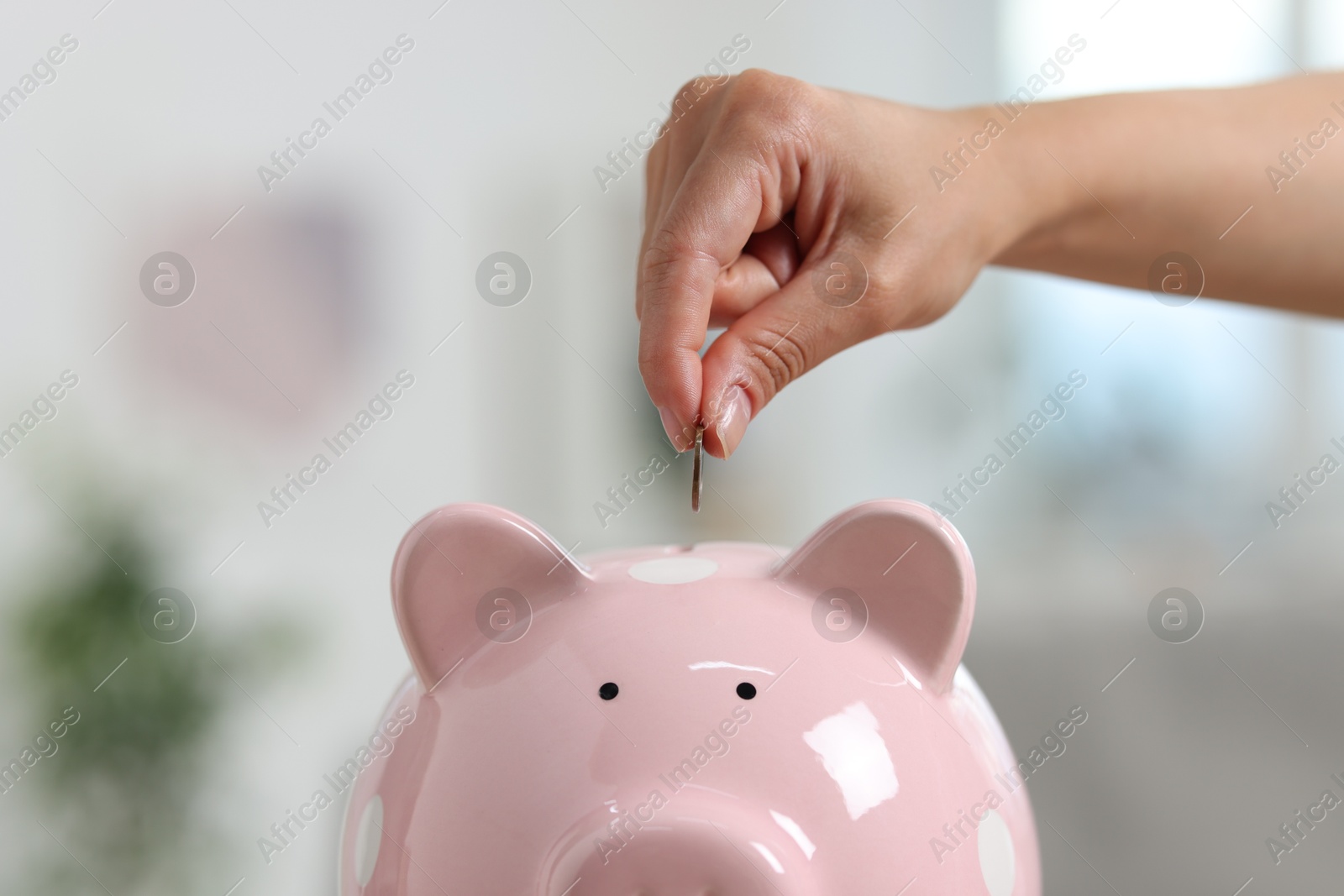 Photo of Woman putting coin into piggy bank against blurred background, closeup