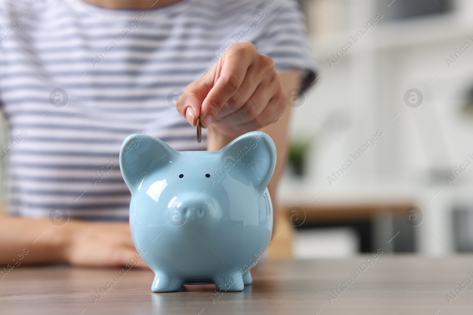 Photo of Woman putting coin into piggy bank at wooden table, closeup