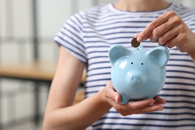 Photo of Woman putting coin into piggy bank indoors, closeup