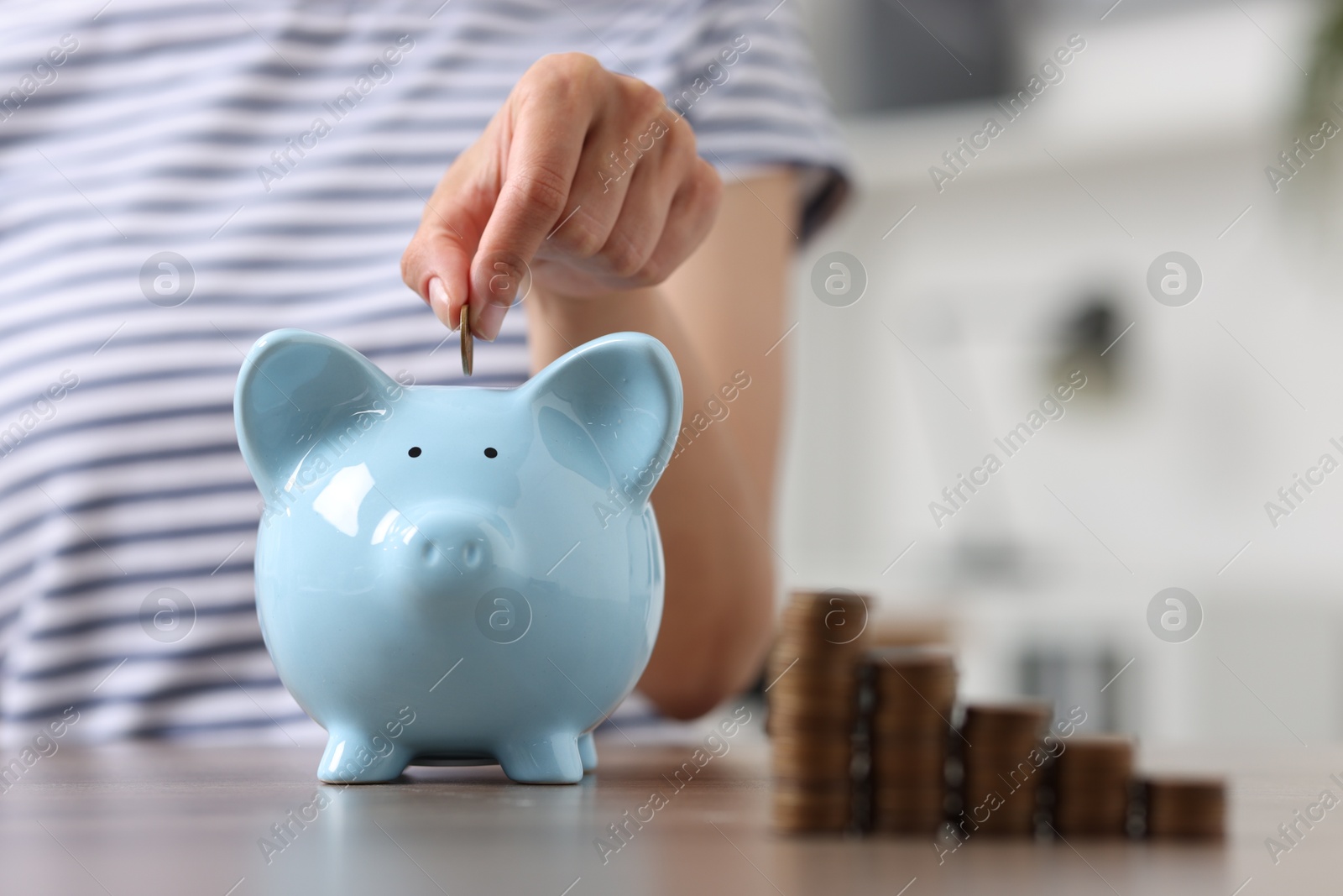 Photo of Woman putting coin into piggy bank at wooden table, closeup