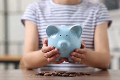 Photo of Woman holding piggy bank over table with coins indoors, closeup