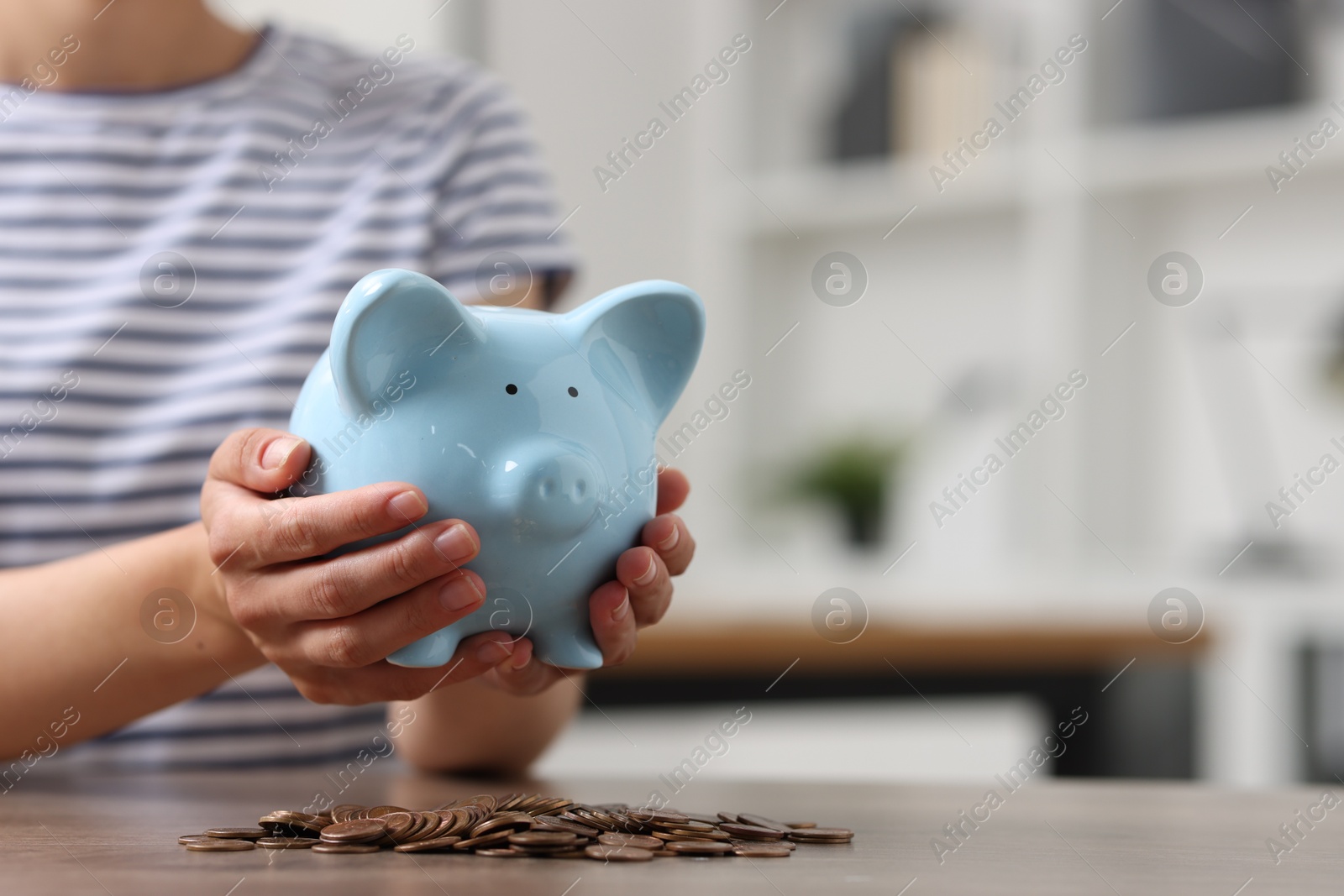 Photo of Woman holding piggy bank over table with coins indoors, closeup