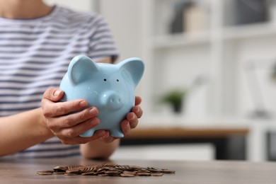 Woman holding piggy bank over table with coins indoors, closeup