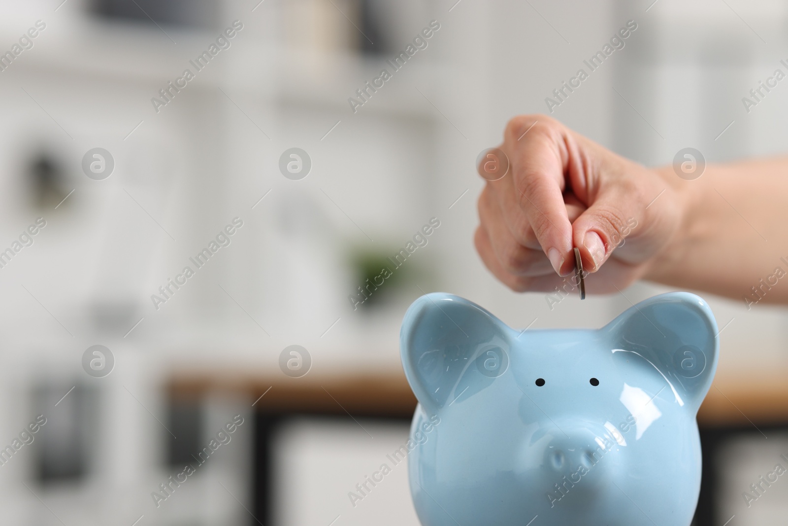 Photo of Woman putting coin into piggy bank against blurred background, closeup. Space for text