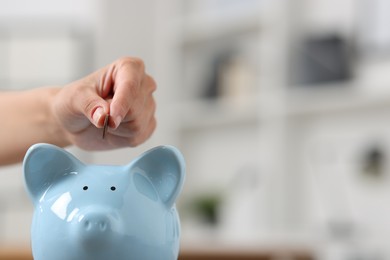 Photo of Woman putting coin into piggy bank against blurred background, closeup. Space for text