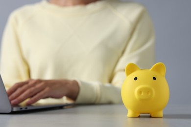 Photo of Woman using laptop at table, focus on piggy bank