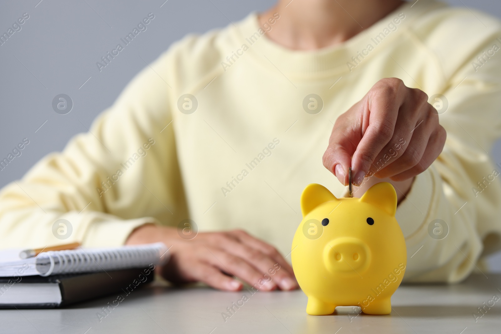 Photo of Woman putting coin into piggy bank at table, closeup