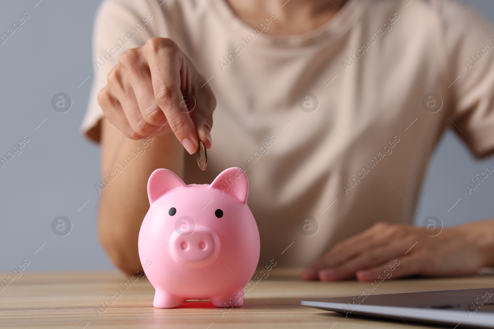 Photo of Woman putting coin into piggy bank at wooden table, closeup