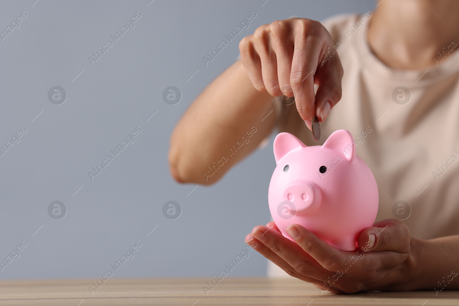 Photo of Woman putting coin into piggy bank at wooden table, closeup. Space for text