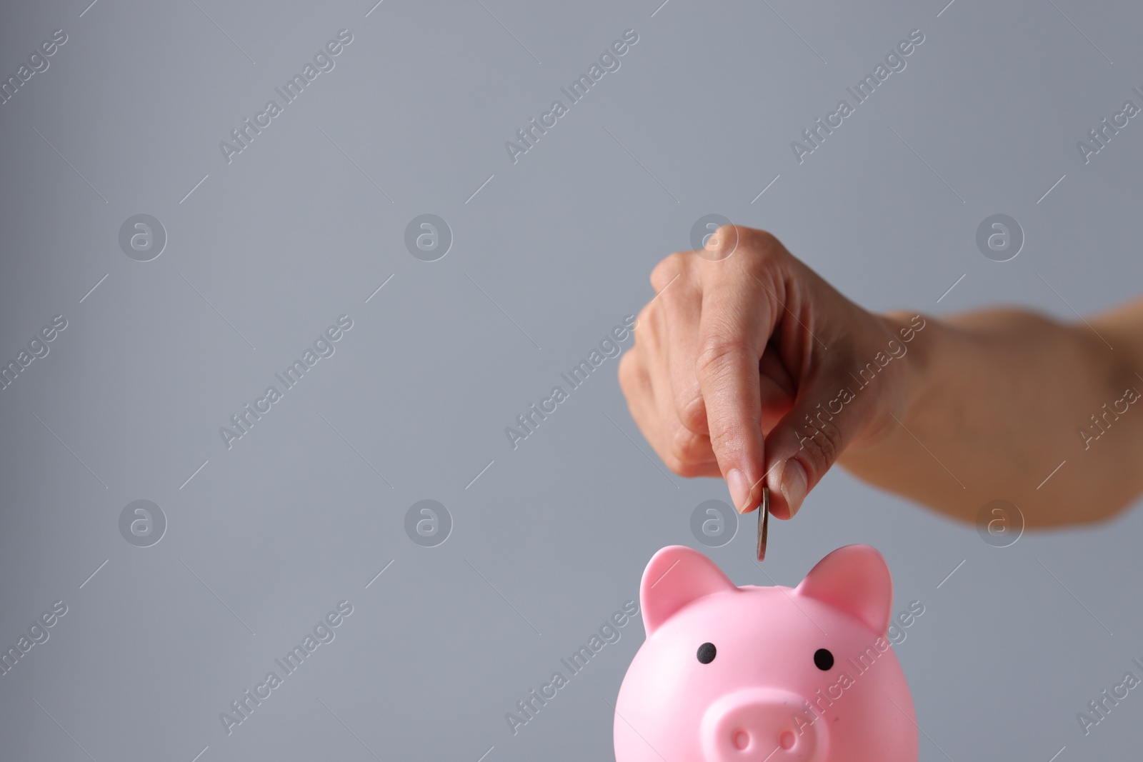 Photo of Woman putting coin into piggy bank against grey background, closeup. Space for text