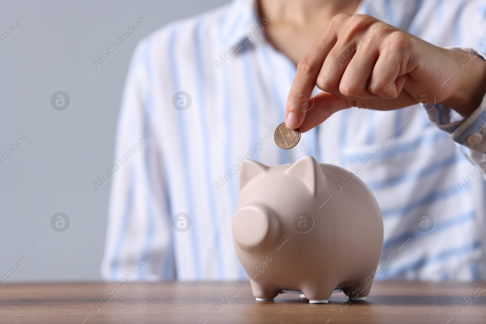 Photo of Woman putting coin into piggy bank at wooden table, closeup