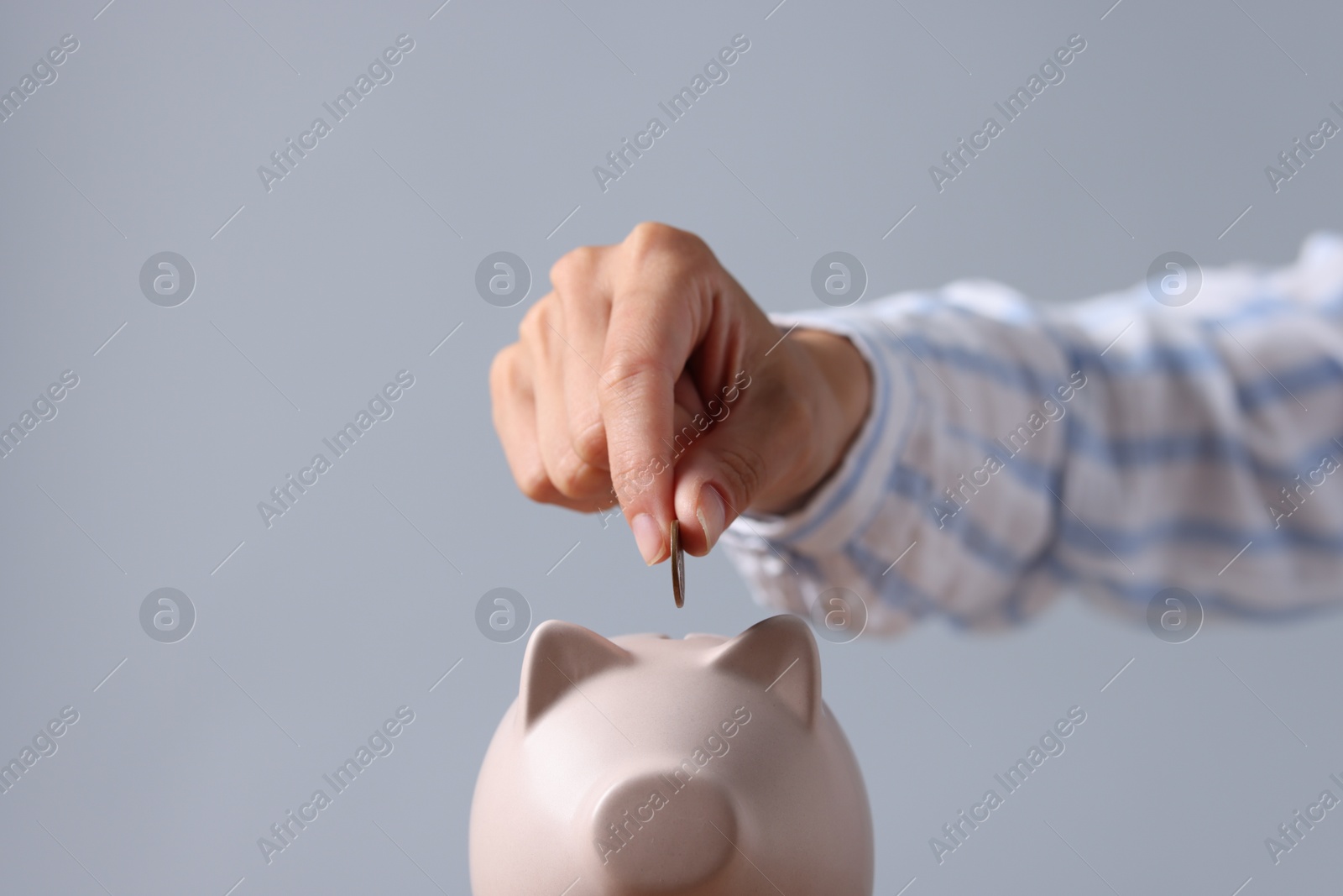 Photo of Woman putting coin into piggy bank against grey background, closeup