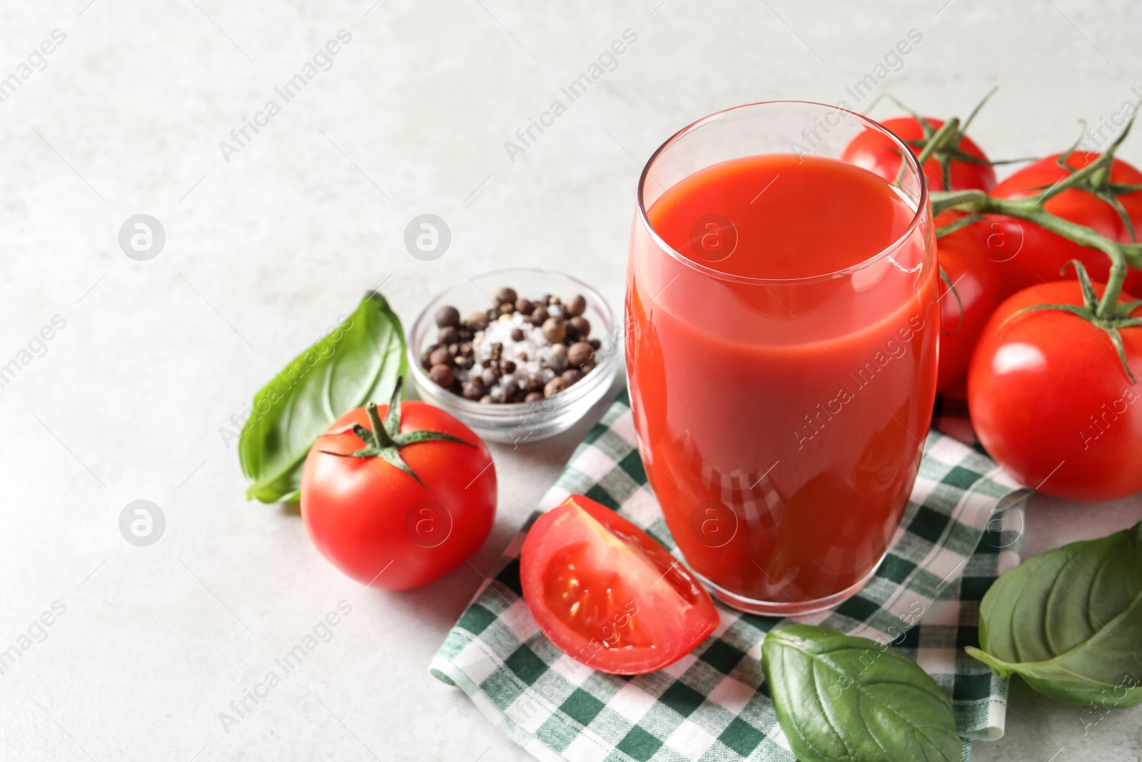 Photo of Tasty tomato juice in glass, spices and fresh vegetables on light table, space for text