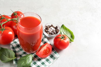 Photo of Tasty tomato juice in glass, spices and fresh vegetables on light table, space for text