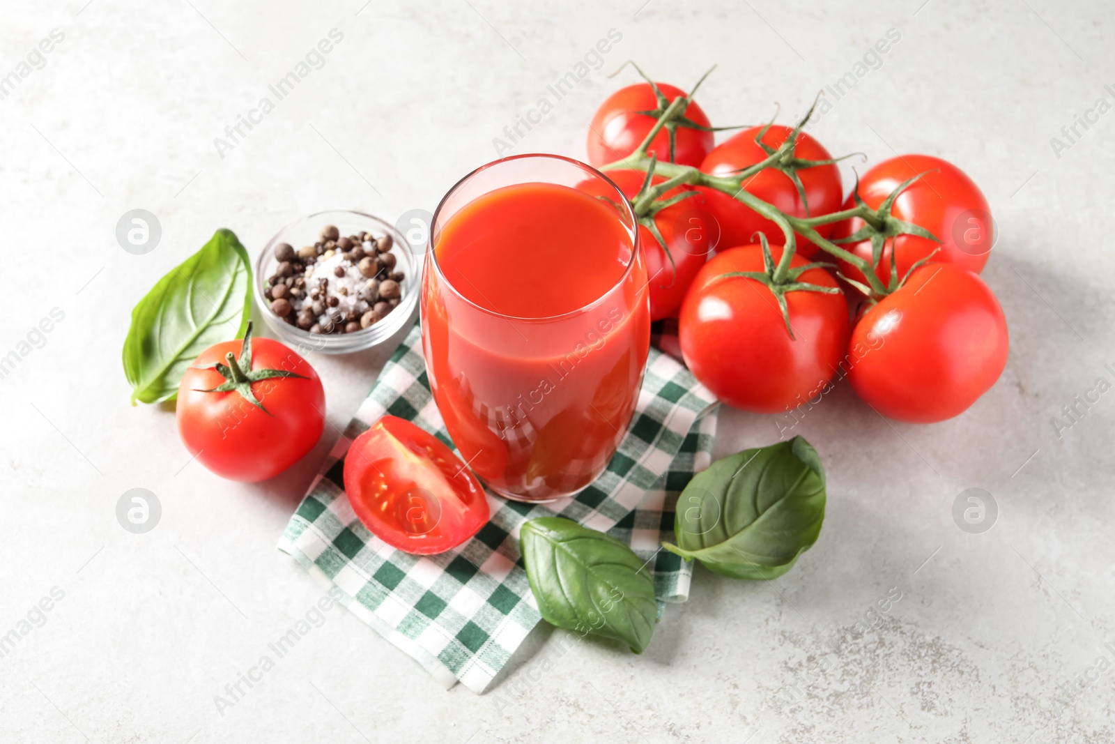 Photo of Tasty tomato juice in glass, spices and fresh vegetables on light table