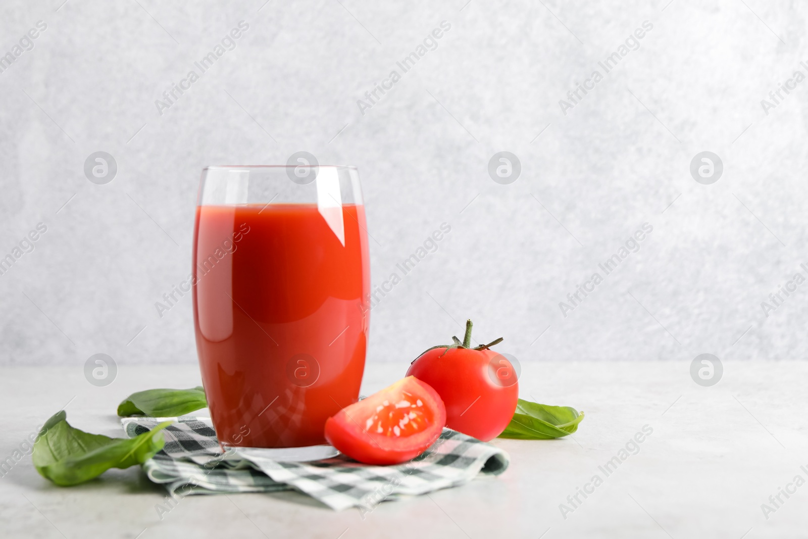 Photo of Tasty tomato juice in glass, basil leaves and fresh vegetables on light table, space for text