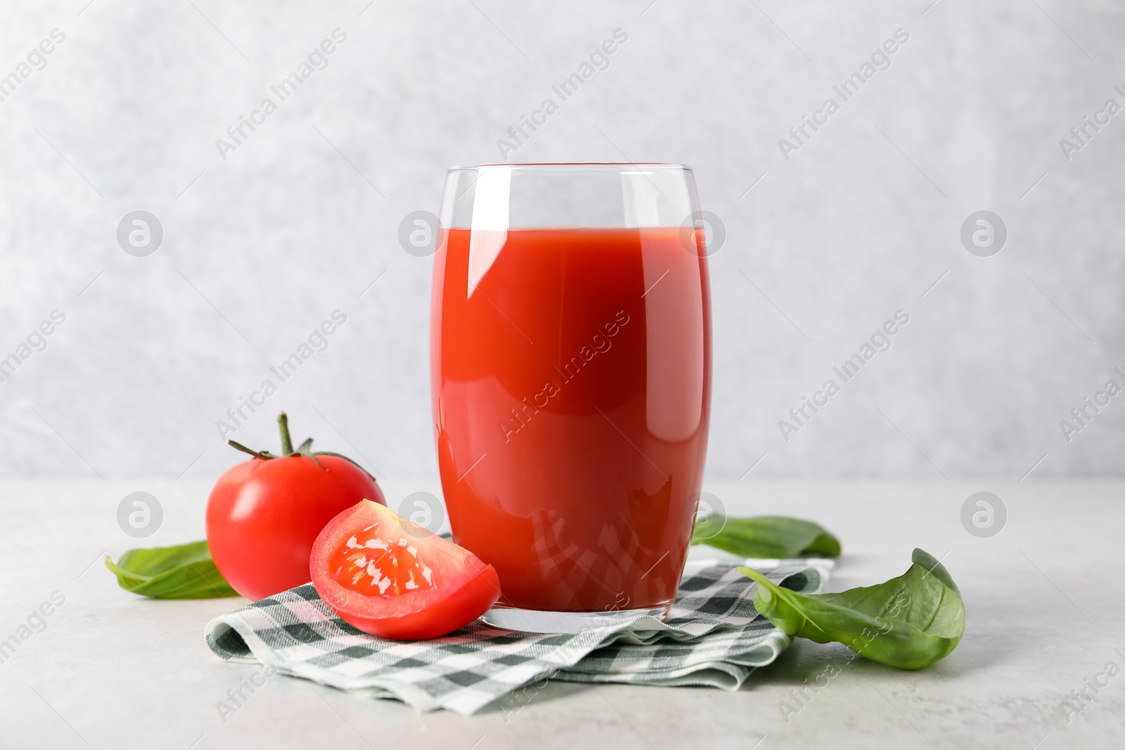 Photo of Tasty tomato juice in glass, basil leaves and fresh vegetables on light table