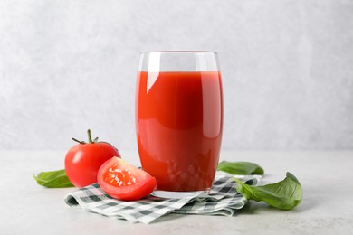 Tasty tomato juice in glass, basil leaves and fresh vegetables on light table