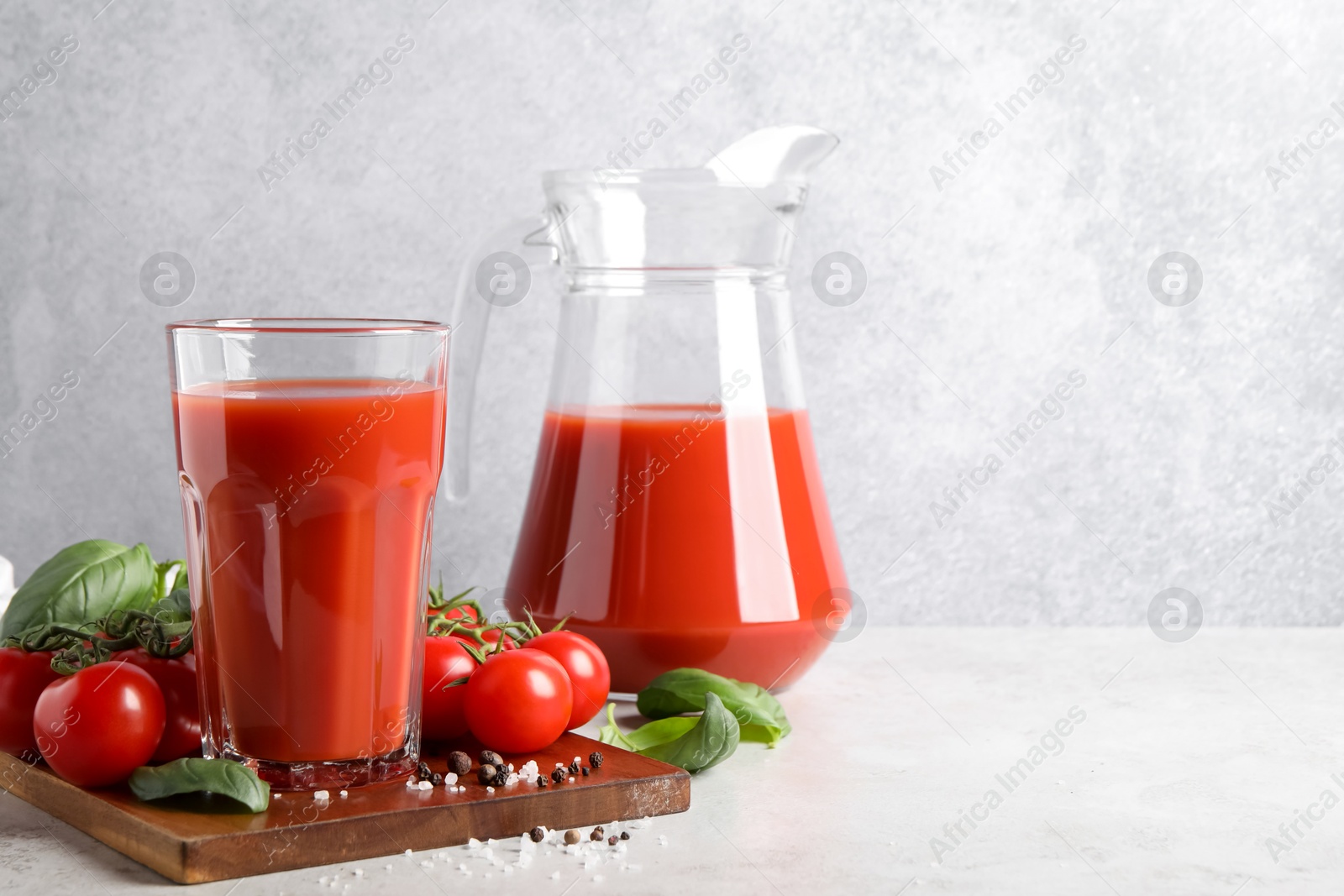 Photo of Tasty tomato juice with spices and fresh vegetables on light table, space for text