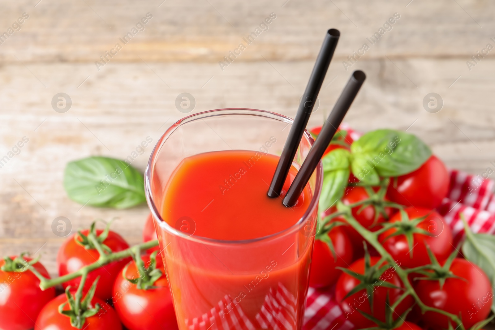 Photo of Fresh tomato juice and straws in glass on table, closeup