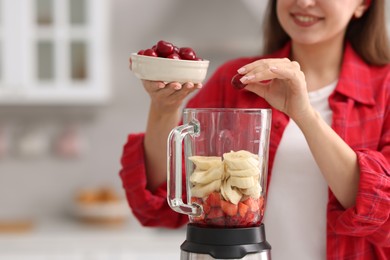 Woman making delicious smoothie with blender in kitchen, closeup