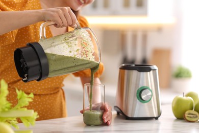 Woman pouring fresh smoothie from blender cup into glass at white marble table in kitchen, closeup