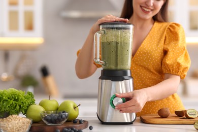 Woman making delicious smoothie with blender at white marble table in kitchen, closeup