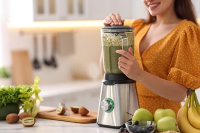 Photo of Young woman making delicious smoothie with blender at white marble table in kitchen