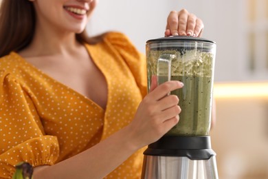 Woman making delicious smoothie with blender in kitchen, closeup