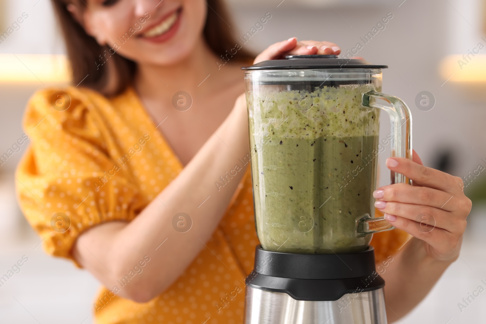 Photo of Woman making delicious smoothie with blender in kitchen, closeup