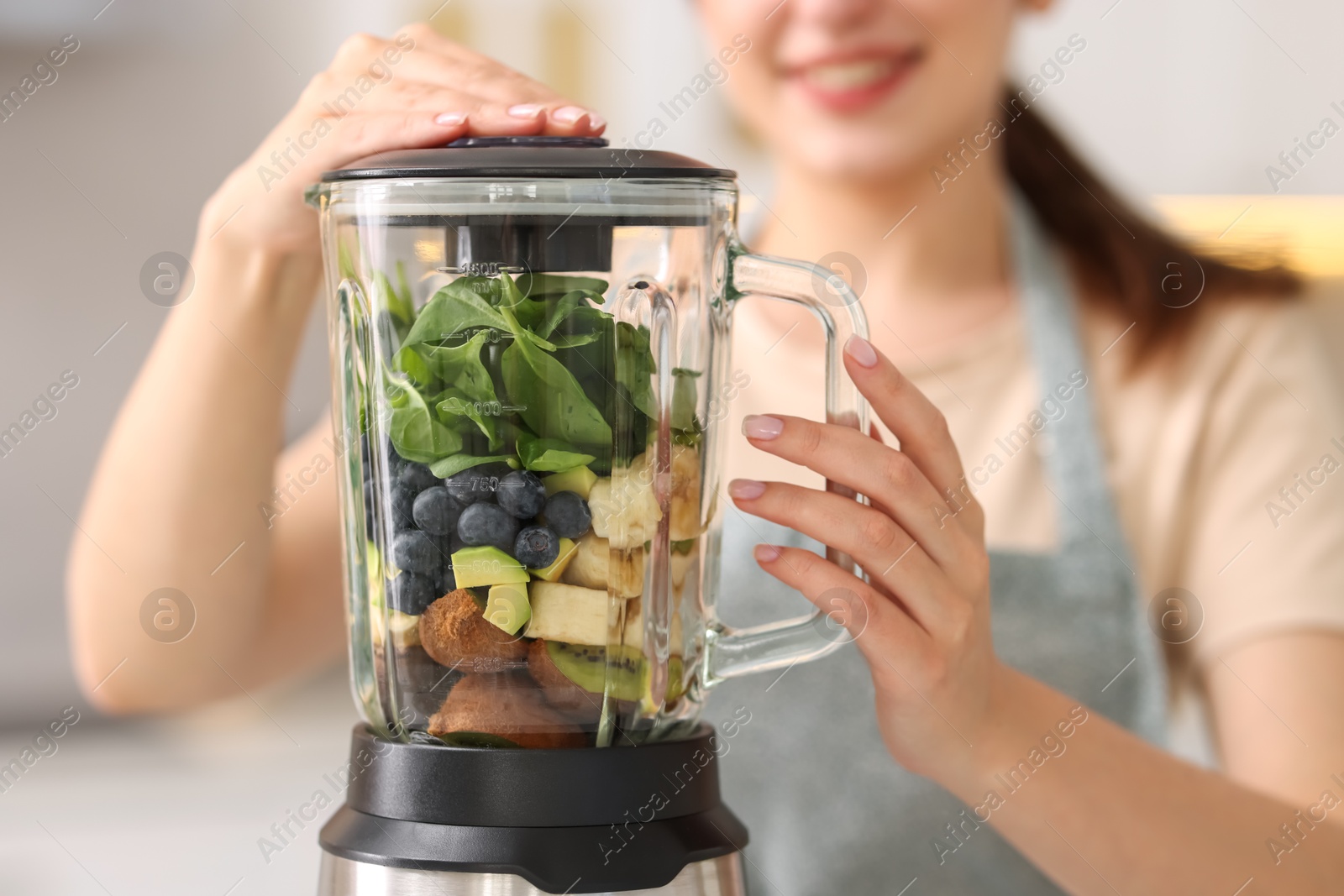 Photo of Woman making delicious smoothie with blender in kitchen, closeup