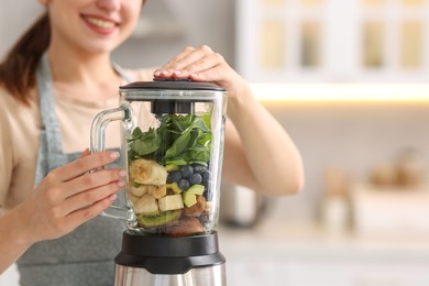 Photo of Woman making delicious smoothie with blender in kitchen, closeup