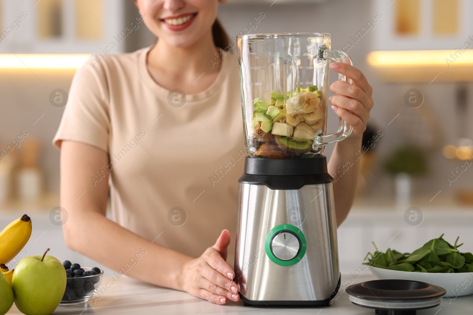 Photo of Woman making delicious smoothie with blender at white marble table in kitchen, closeup