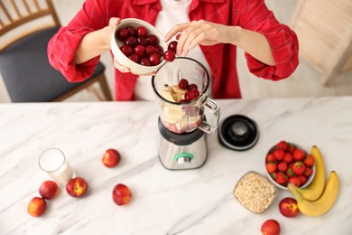 Photo of Woman making delicious smoothie with blender at white marble table in kitchen, closeup