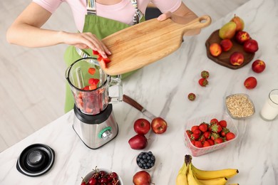 Photo of Woman making delicious smoothie with blender at white marble table in kitchen, above view