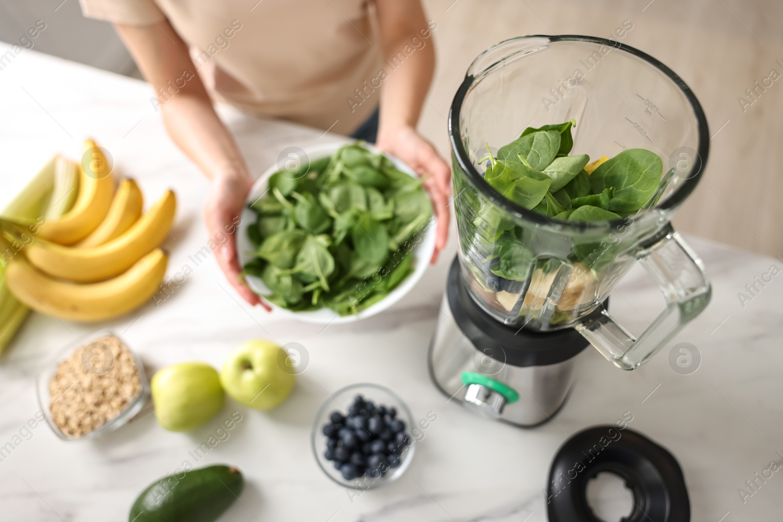 Photo of Woman making delicious smoothie with blender at white marble table in kitchen