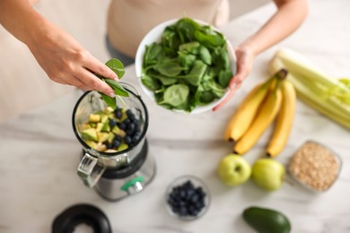 Photo of Woman making delicious smoothie with blender at white marble table in kitchen, above view